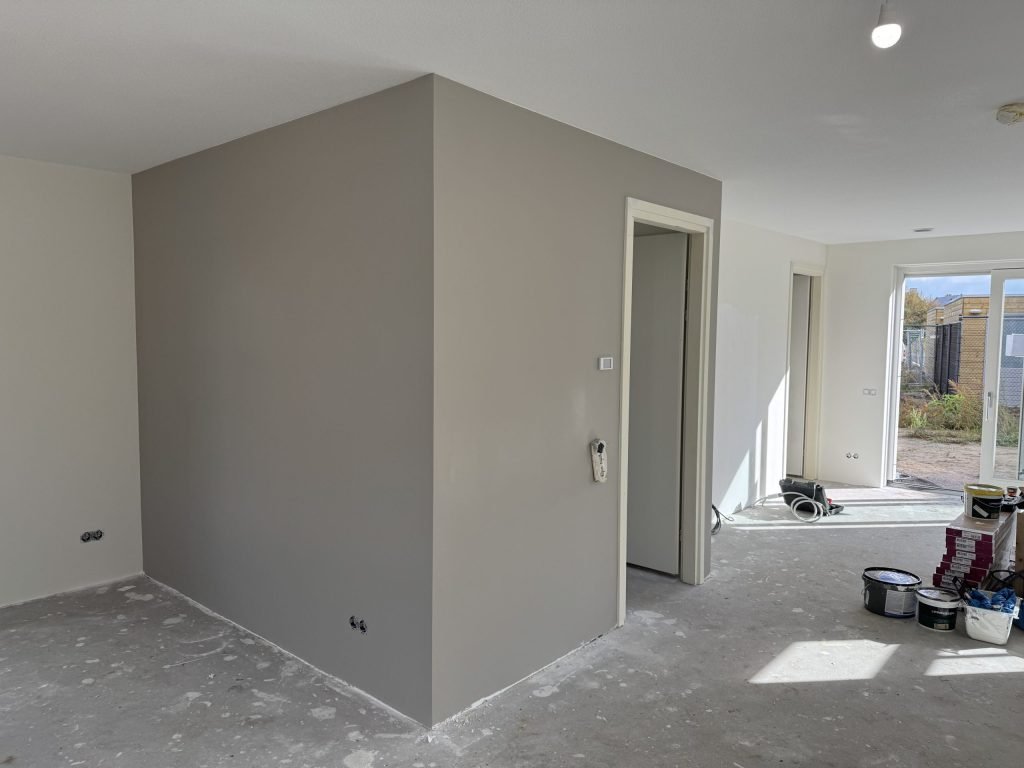 Nieuwbouwwoning tijdens de afwerking: een grijze muurkolom, witte wanden en verfemmers op de betonvloer