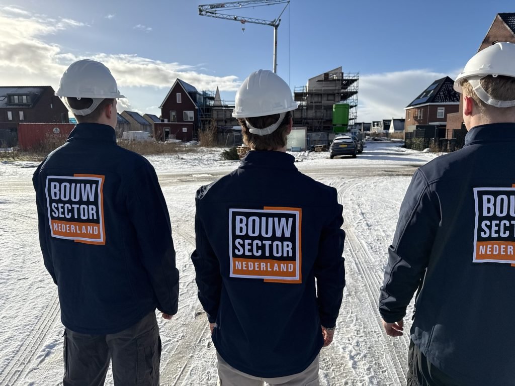 Drie vakmensen van Bouwsector Nederland met witte helm op een besneeuwde bouwplaats met een kraan